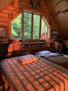 two beds in a room with wooden walls and flooring, windows overlooking the woods