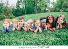 a group of children laying in the grass with their hands on their faces and smiling