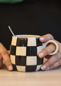 two hands holding a black and white checkered coffee cup