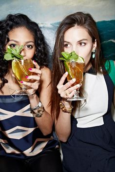 two beautiful young women holding up glasses filled with liquid and green leafy drinks in front of their faces