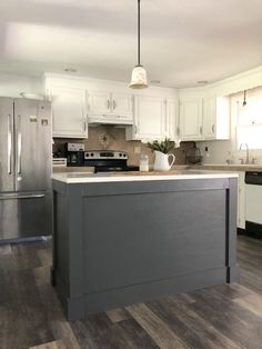 a kitchen with white cabinets and gray island in the center, stainless steel refrigerator and dishwasher