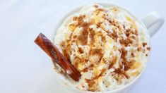 a white cup filled with whipped cream and cinnamon on top of a saucer next to a spoon