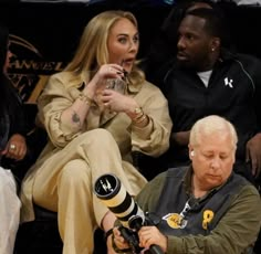 a woman sitting on top of a basketball court next to an older man holding a camera