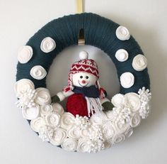 a snowman wreath with white flowers and a knitted hat hanging on the wall