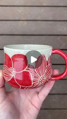 a hand holding a red and white coffee cup with flowers on the inside, in front of a wooden wall