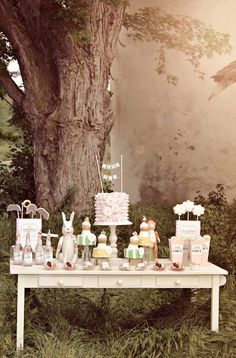 a table topped with lots of cakes and cupcakes next to a large tree