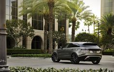 a silver land rover parked in front of a tall building with palm trees and bushes