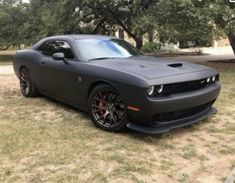 a black car is parked in the grass near some trees and bushes, it's dark gray with red rims