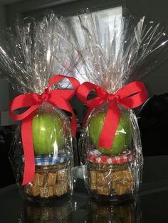 two clear plastic bags with apples in them and some candy wrapped in red ribbon on top