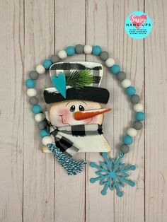 a snowman with a hat and scarf on a beaded bracelet that is hanging from a wooden wall