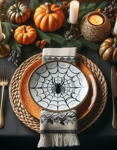 a place setting with pumpkins, candles and spiderweave napkins on it