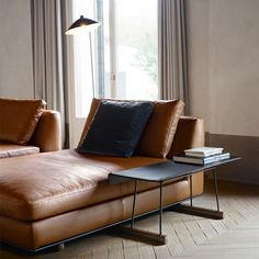 a brown leather couch sitting in front of a window next to a table with books on it