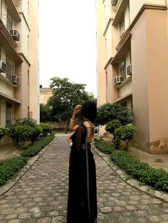 a woman in a long black dress is standing on a brick walkway between two buildings