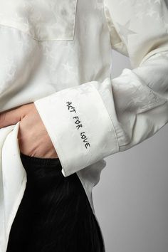 a person wearing a white shirt with writing on the chest and black pants, holding their hand in his pocket