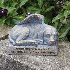 a statue of a dog laying on top of a rock next to some plants and flowers