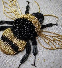 a black and gold bee is sitting on a piece of white fabric with golden thread