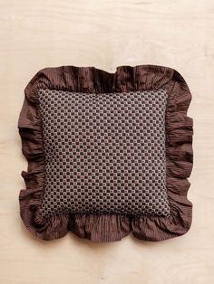 a brown and black pillow with ruffles on it sitting on a wooden surface