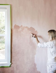 a woman is painting the wall with pink paint