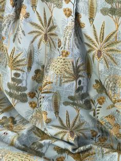 a close up view of a blue and gold patterned fabric with trees, flowers, and leaves on it