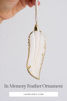 a hand holding a white ornament with the words in memory feathered ornament