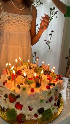 a woman standing in front of a cake with candles on it and flowers around the edges