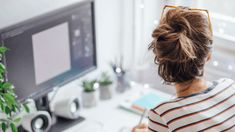 a woman sitting in front of a computer monitor with her hair pulled back into a bun