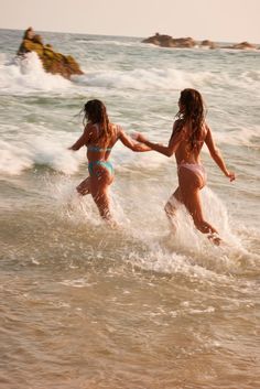 two women in bikinis are running through the ocean water on their surfboards and holding hands