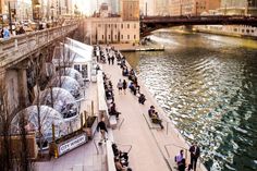 people are walking on the sidewalk next to the water and buildings in the background,