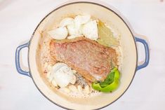 meat, potatoes and peppers in a pot on a white tablecloth with a blue rim