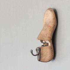 an old wooden shoe with a hook on it's side against a gray wall