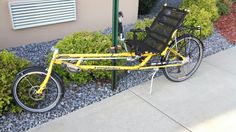 a yellow bicycle parked on the side of a road next to a green pole and bushes