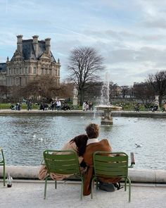 two people sitting on green chairs in front of a fountain