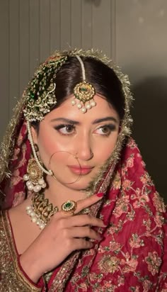 a woman wearing a red and gold bridal outfit with jewelry on her head, posing for the camera