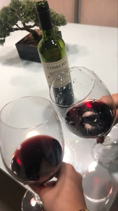 two glasses of red wine are being held by someone's hand while sitting at a table