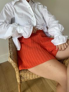 a woman sitting in a chair wearing a white shirt and orange knitted miniskirt