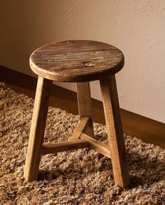 a wooden stool sitting on top of a shaggy rug next to a wall and floor