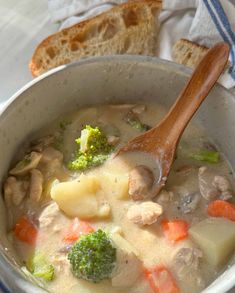 a wooden spoon in a bowl filled with soup and broccoli next to some slices of bread