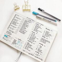 an open planner with pens and paper clips next to it on a white table top