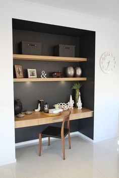 a desk and chair in a room with shelves on the wall above it, along with a clock