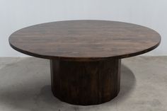 a round wooden table sitting on top of a cement floor next to a white wall