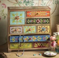 an assortment of colorful painted drawers on a table with flowers in vases next to it