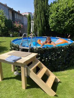 a woman laying in an above ground pool next to a wooden table and ladders