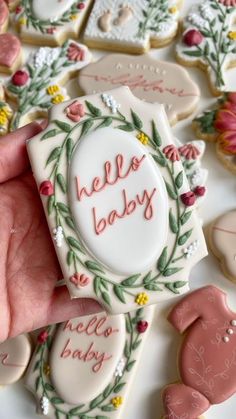 a hand holding a hello baby decorated cookie in front of some cookies on the table