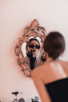 a woman is looking at her reflection in the mirror while wearing black gloves and pearls