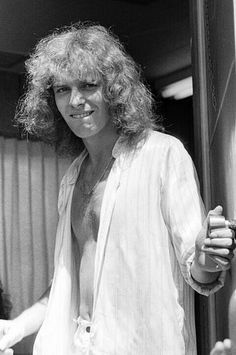 a man with long hair standing in front of a door and holding a glass bottle