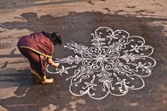 a woman is drawing on the ground with chalk