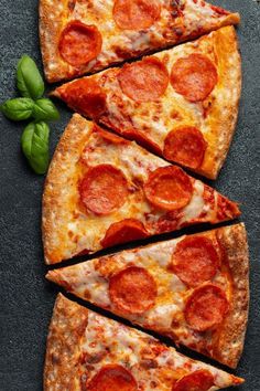 several slices of pepperoni pizza are arranged on a black surface with basil leaves nearby