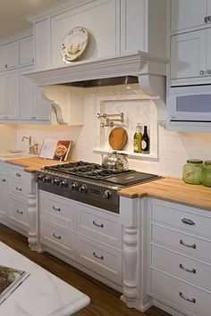 a kitchen with white cabinets and wood counter tops, an oven hood over the stove