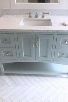 a bathroom vanity with two sinks and a mirror in the backround, along with herringbone tile flooring