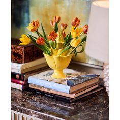 a yellow vase filled with lots of flowers on top of a table next to books